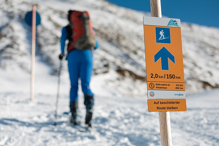 Beschilderung und im Hintergrund eine Frau in Pistenmontur 