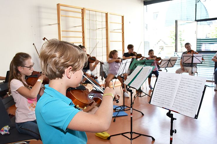 Gruppe von Kindern mit Streichinstrumenten, im Vordergrund ein Junge Geige spielend