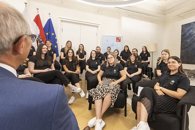 Die zwei Schülerinnen Leonie Bangheri und Valentina Madreiter sitzen vor LH Mattle und stellen ihm die ausgearbeiteten Fragen.