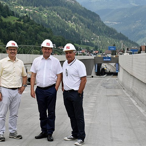 Der Leiter des Baubezirksamts Imst Bernd Stigger steht links neben Landeshauptmann-Stellvertreter Josef Geisler. Rechts neben dem Landeshauptmann-Stellvertreter steht Bürgermeister Heinz Kofler. Die drei Männer stehen vor der Baustelle der Unterführung.