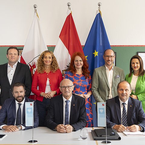 Alle Mitglieder der Tiroler Landesregierung auf einem Gruppenbild mit der österreichischen, tiroler und europäischen Flagge im Hintergrund.