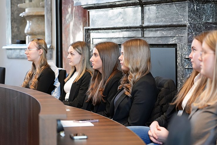 Mehrere junge Frauen sitzen im Landtagssaal auf einer Bank. 