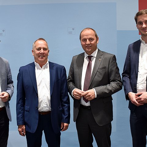 Gruppenfoto der vier Teilnehmer an der Pressekonferenz vor blauem Hintergrund mit Tirol Logo am rechten oberen Rand.