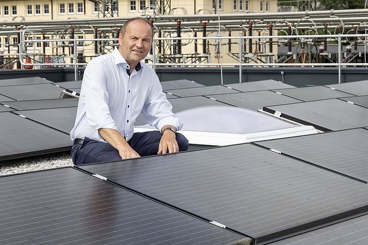 LHStv Geisler kniet zwischen PV-Paneelen auf Dach eines Gebäudes