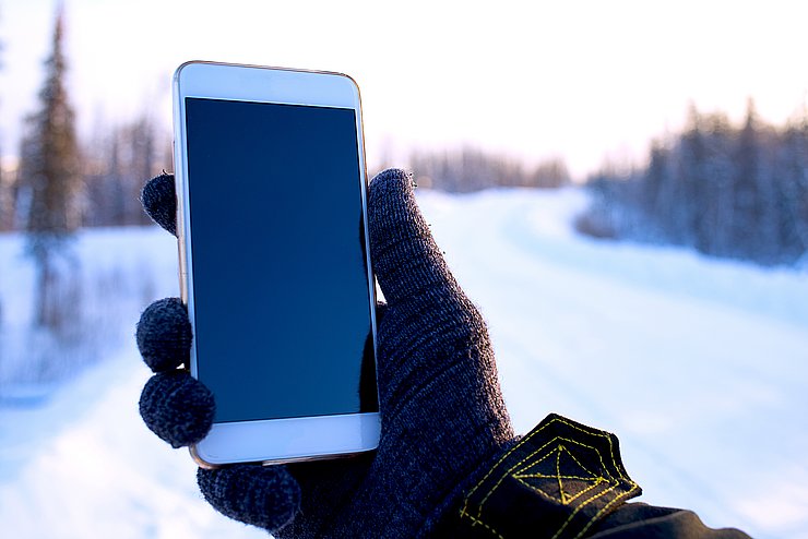 Hand hält Mobiltelefon in einer winterlichen Umgebung