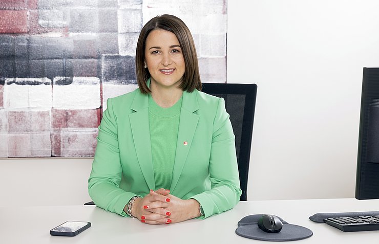 Mair mit grünen Blazer an Schreibtisch sitzend