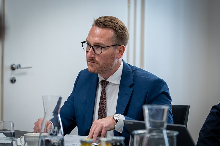 Wohlgemuth blickt über einen Tisch nach links.