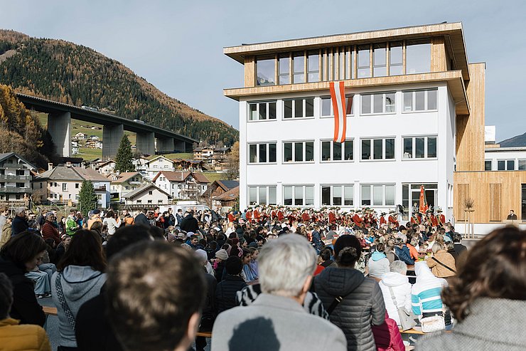 Schulgebäude mit Fahne, davor Festgesellschaft