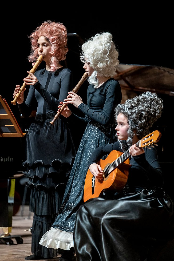 Drei Mädchen musizieren in Perücken.