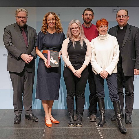 Personen stehen nebeneinander, LRin hält Buch in Händen