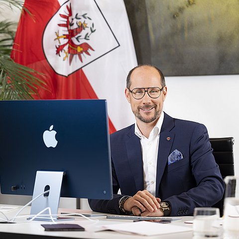 Mario Gerber sitzt am Schreibtisch vor Computer mit Blick in die Kamera