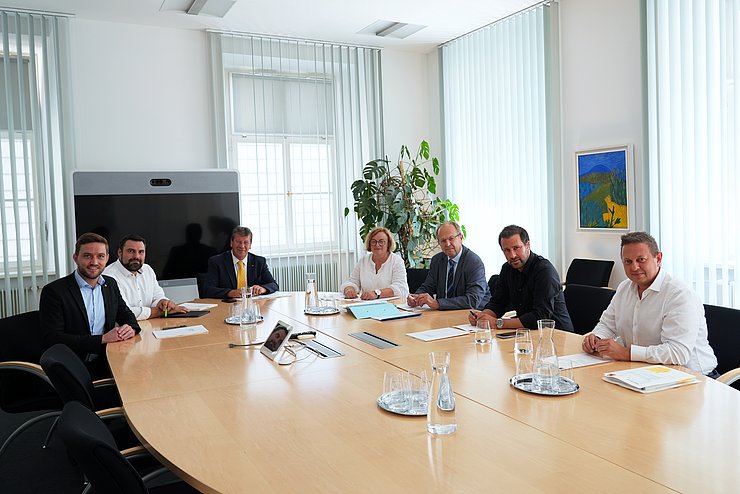 Die Mitglieder des Wohnbauförderungskuratoriums sitzen bei ihrer jüngsten Sitzung im Landhaus in Innsbruck um einen ovalen Tisch schauen für das Gruppenfoto in die Kamera