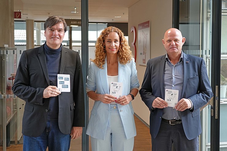 Personen stehen nebeneinander, halten Flyer des Sozialroutenplans