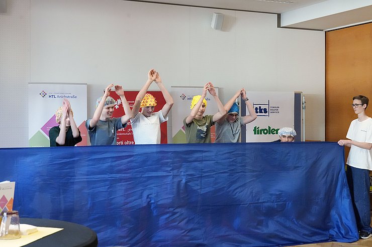 © Land Tirol/Reiter SchülerInnen mit Bademasken heben Hände hoch, davor blaues Tuch (steht für Wasser)