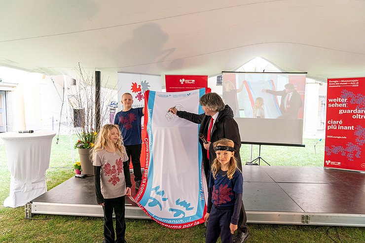 Kinder halten Tuch, Mann schreibt darauf