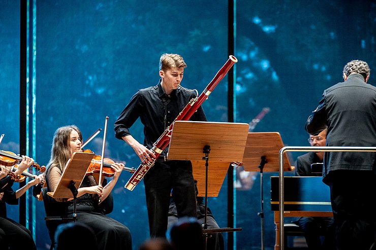 Ein junger Mann spielt auf einer Bühne Fagott.