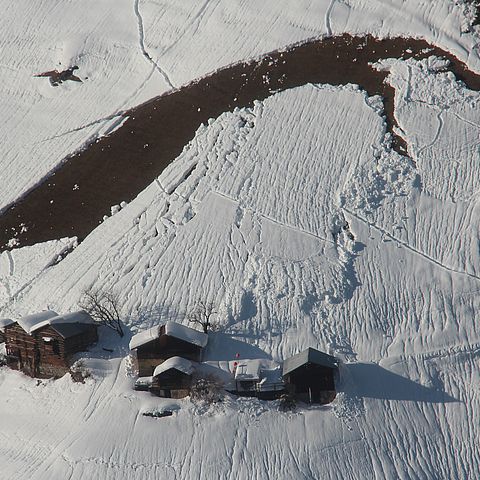 Gleitschnee auf steilem Wiesenhang bedroht Häuser in der Region Silvretta/Samnaun.