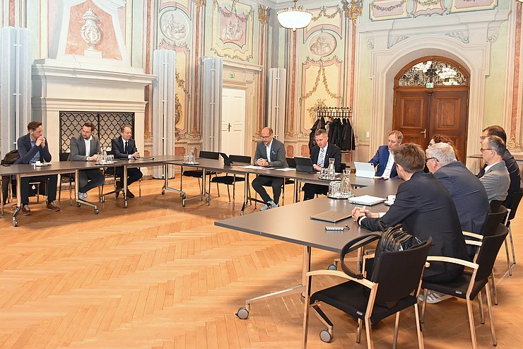 Einige Menschen hocken hinter Tischen in U-Form und besprechen sich.