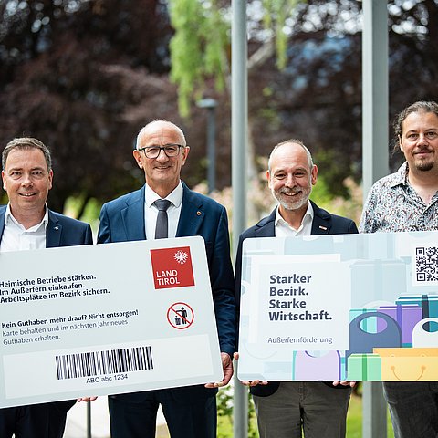 Vier Männer halten die Vorder- und Rückseite eines Riesen-Einkaufsgutscheines in der Hand.