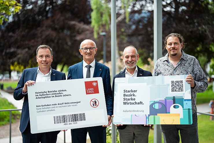 © Land Tirol/Fitsch Vier Männer halten die Vorder- und Rückseite eines Riesen-Einkaufsgutscheines in der Hand.