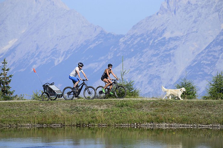 © Land Tirol/Noichl Mann und Frau auf Rad auf einem Berg mit Hund, der vorausläuft