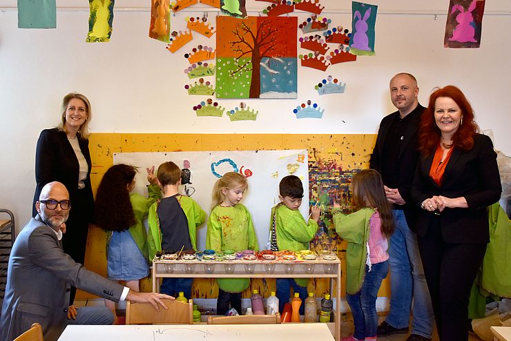 Gruppenfoto von Personen im Kindergarten, Kinder malen mit Farben ein Bild an der Wand