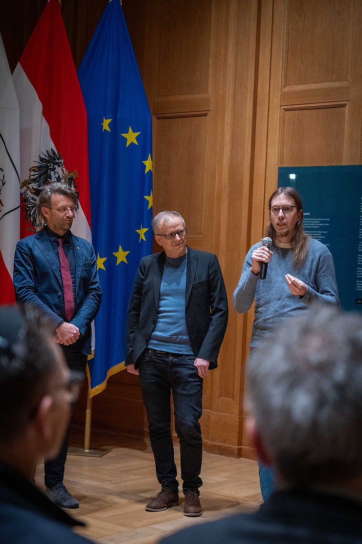 Drei Männer vor Fahnen.