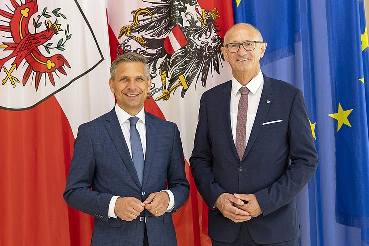 Zwei Menschen posieren vor mehreren Flaggen.