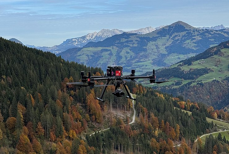 © Land Tirol/Drohnen-Einsatz-Gruppe Fliegende Drohne mit Land Tirol Logo vor Bergkulisse.