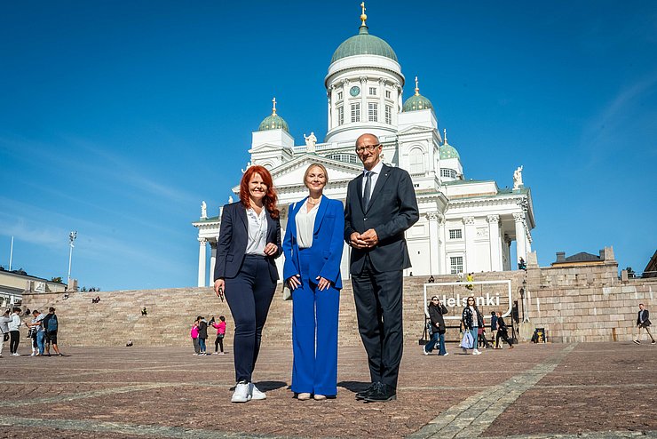 Gruppenfoto auf Platz vor großem weißenm Gebäude mit grünen Dächern