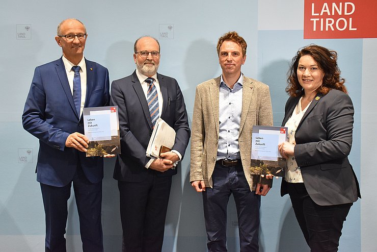 Gruppenfoto der vier Personen stehend vor hellblauem Hintergrund. 