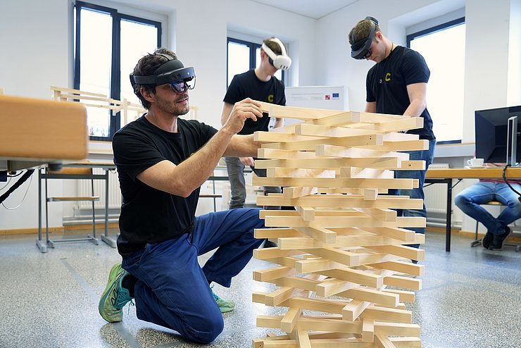 drei Personen mit VR-Brille bauen einen Holzturm