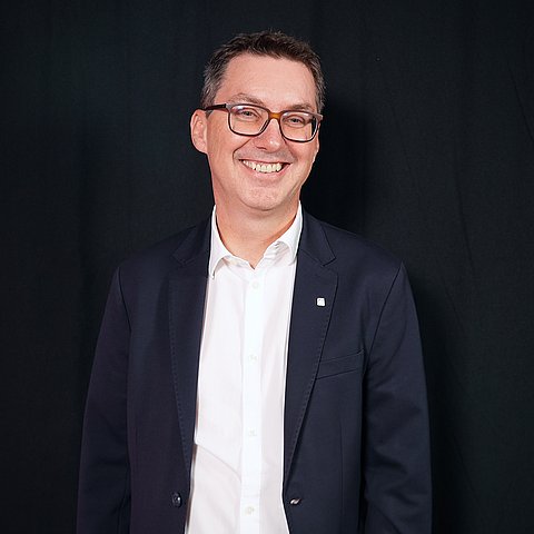 Mann im Anzug mit Brille vor schwarzer Wand
