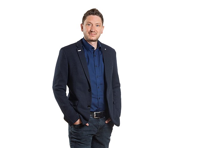 Ein Mann steht aufrecht und schaut direkt in die Kamera.
