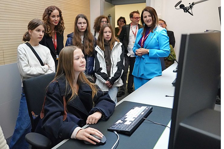 Mädchen an Computer, Personen stehen dahinter