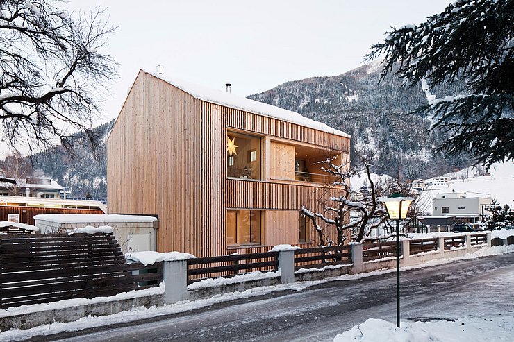 © © Christian Flatscher Holzhaus neben Straße, die mit Schnee bedeckt ist