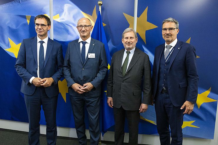 Gruppenfoto: Die vier Herren in dunklen Anzügen mit Krawatte; im Hintergrund eine Wand mit aufgeklebter EU-Fahne und großen gelben Sternen auf blauen Hintergrund