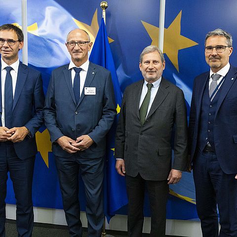 Gruppenfoto: Die vier Herren in dunklen Anzügen mit Krawatte; im Hintergrund eine Wand mit aufgeklebter EU-Fahne und großen gelben Sternen auf blauen Hintergrund