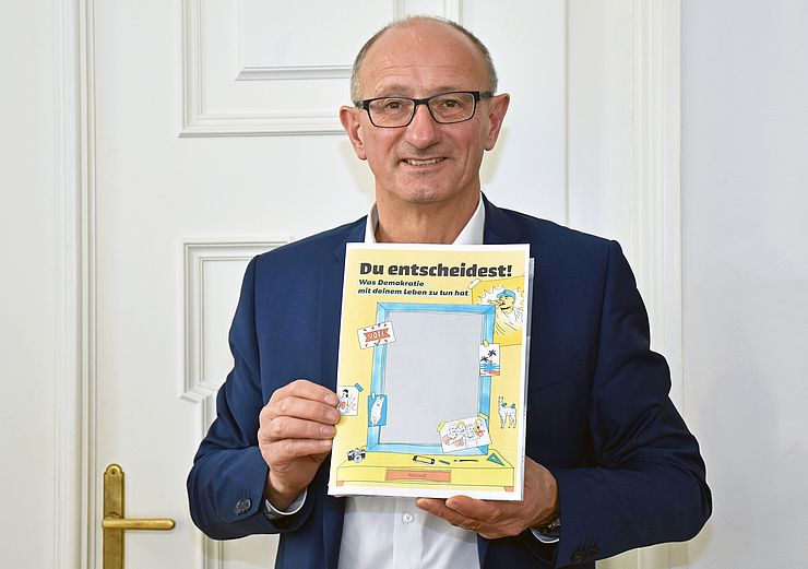 Jugendlandesrat Anton Mattle mit dem Deckblatt der Demokratiebroschüre „Du entscheidest!“ der österreichischen Jugendinfos.