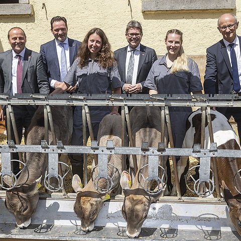 Alle Gesprächspartner des Podiums stehen gemeinsam mit zwei Veterinärmedizinstudentinnen hinter Kühen, die fressen.