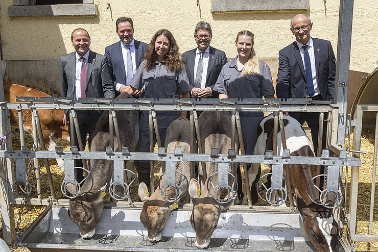 Alle Gesprächspartner des Podiums stehen gemeinsam mit zwei Veterinärmedizinstudentinnen hinter Kühen, die fressen.