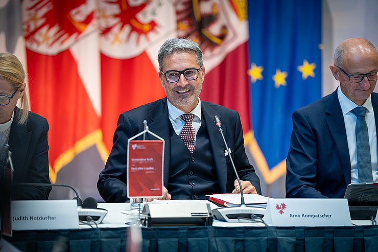 Kompatscher lacht und blickt über den Tisch hinweg.