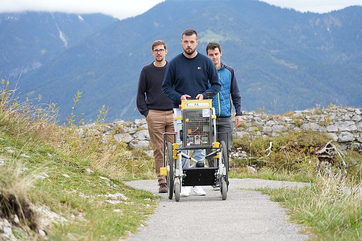 © Land Tirol/Brandhuber Drei Männer gehen hinter Messrollstuhl auf Wanderweg