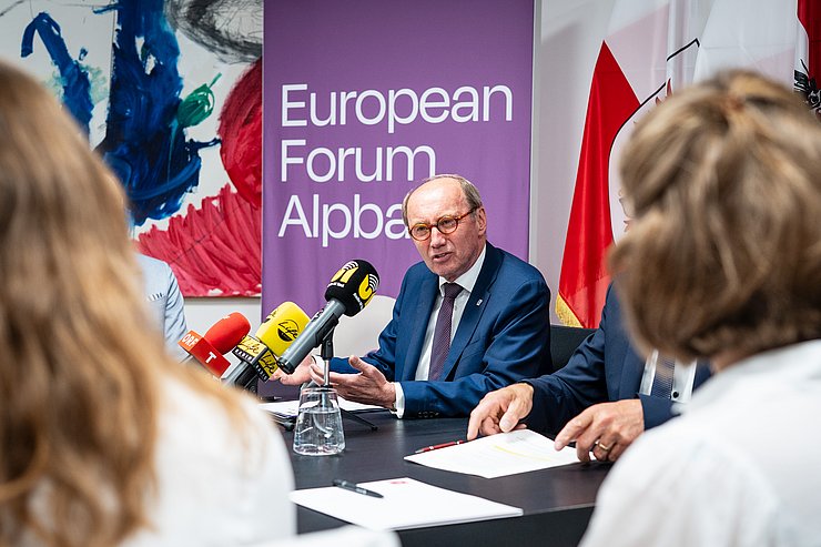 © Land Tirol/Fitsch Karas redend; im Hintergrund Fahnen und ein Roll Up des EFA, vor ihm auf dem Tisch Mikrofone