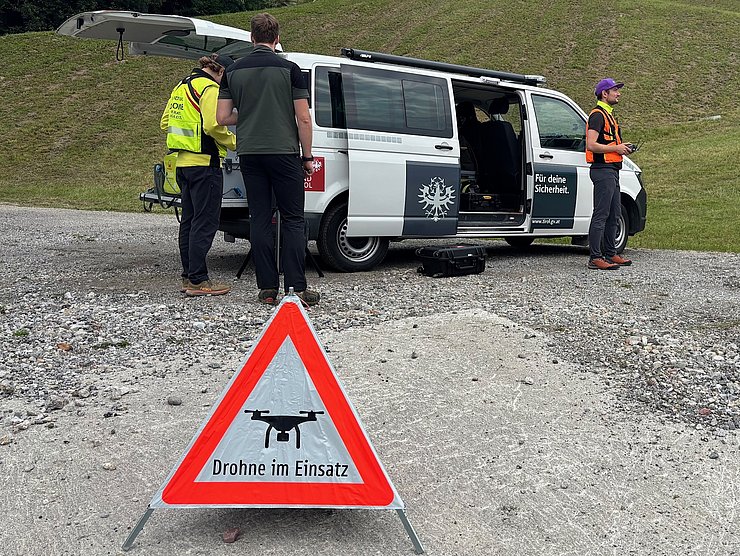 © Land Tirol/Drohnen-Einsatz-Gruppe Einsatzfahrzeug mit Personen und Warndreieck mit Schriftzug Drohneneinsatz