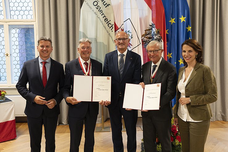 © Land Tirol/Sedlak Fünf Personen, darunter eine Frau, stehen vor Fahnen.