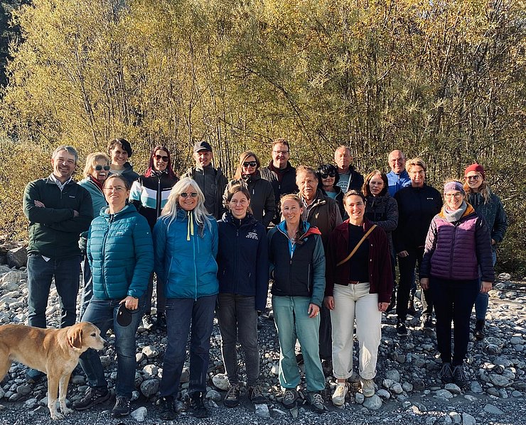 Ein Gruppenbild von verschiedenen Menschen. Sie stehen dicht nebeneinander auf einem steinigen Untergrund im Freien und blicken in die Kamera. Eine Person hält einen Hund an der Leine.