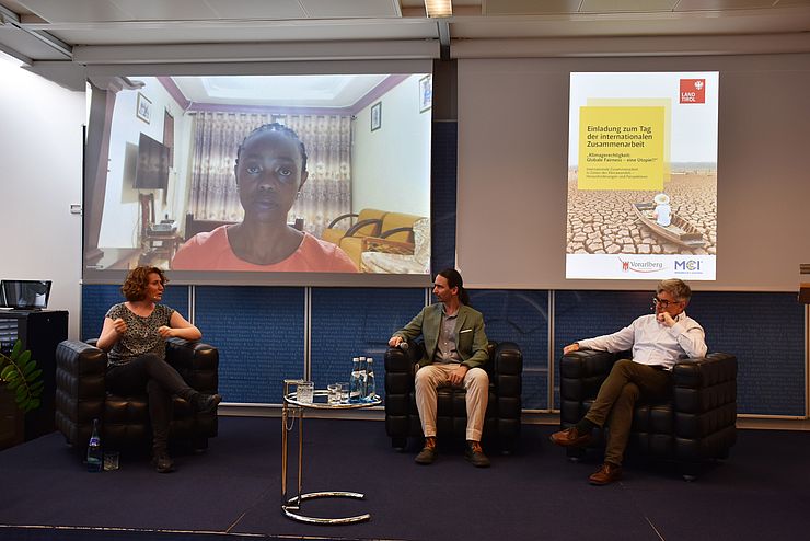 Am Podium sprechen Katharina Rogenhofer, Martin Krenn und Friedbert Ottacher. Susan Nanduddu ist aus Uganda auf einem großen Bildschirm zugeschaltet