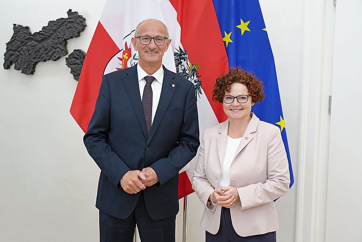 Zwei Menschen posieren vor mehreren Flaggen.