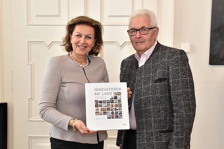 Landesrätin Zoller-Frischauf steht neben Dr. Piock und hält das Buch mit dem Titel "Innovatoren am Land" in der Hand.